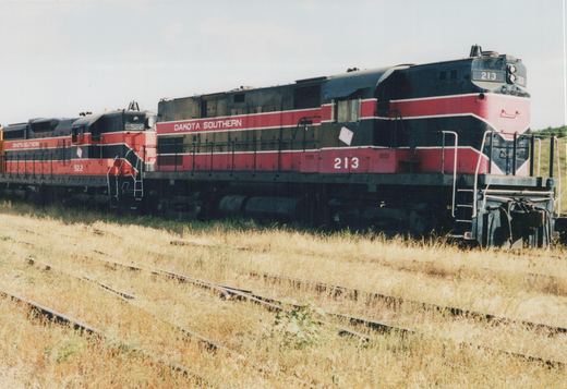 Two red and black Dakota Southern diesel locomotives, numbered 213 and 522, are parked on parallel tracks in a field of dry grass.
