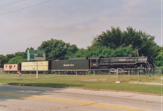 A black steam locomotive numbered 624, labeled Nickel Plate Road, sits on display behind a chain-link fence next to a road, with green trees and a sign for Hammond Civic Center in the background.