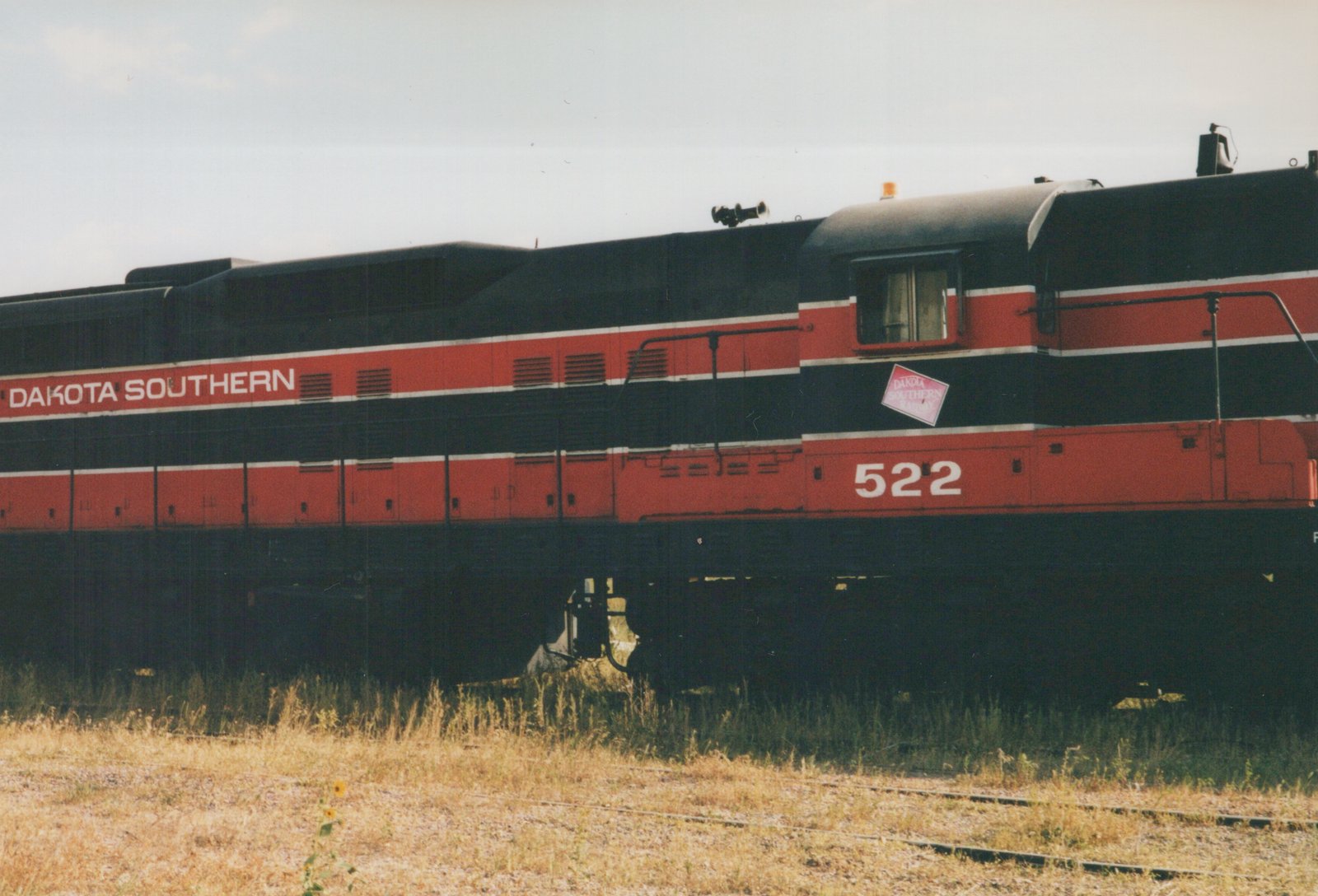 A diesel locomotive with 'Dakota Southern' lettering and the number 522 on its side, standing on a railway track beside dry grass under a clear sky.
