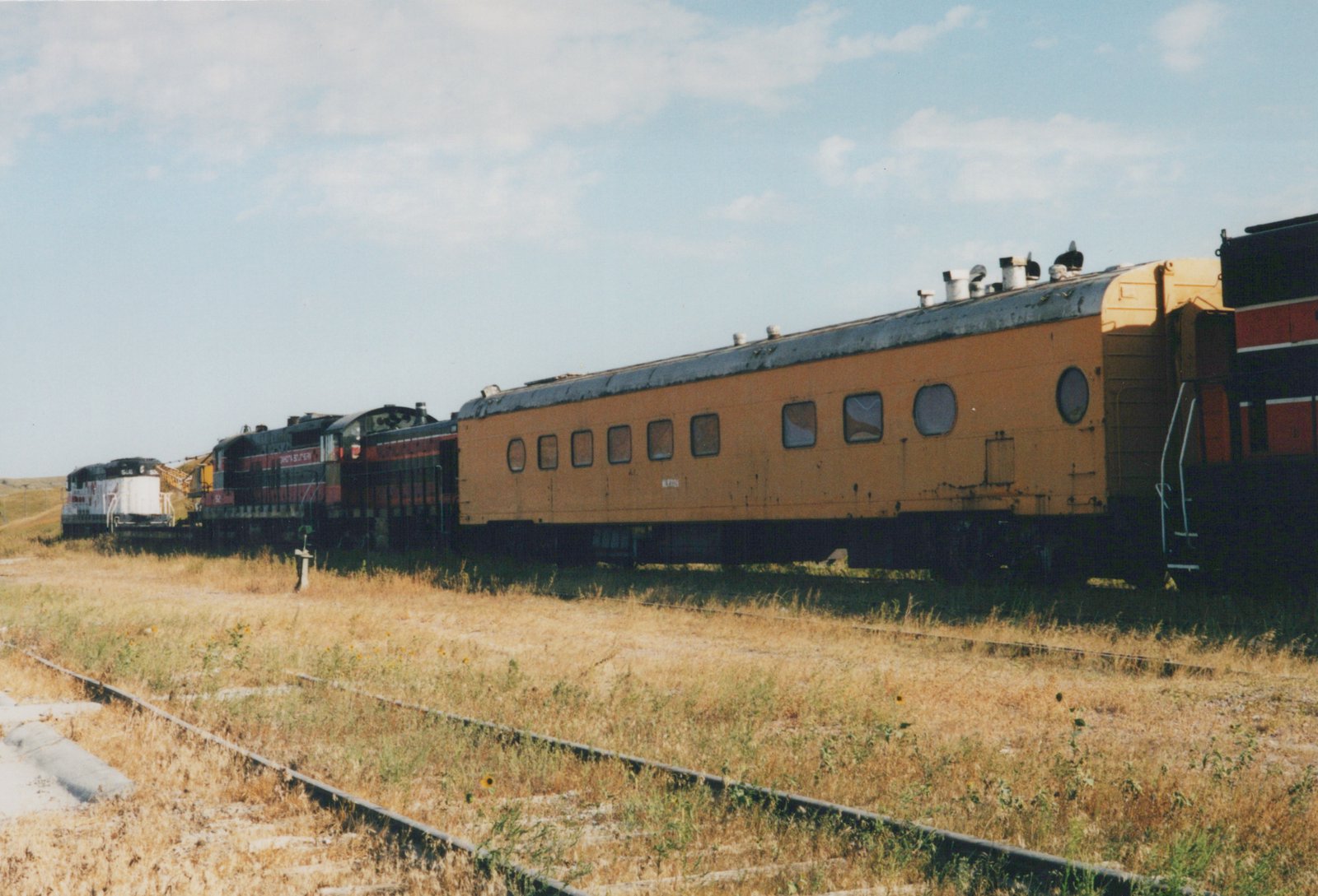 A side view of a North Southern train with two diesel locomotives pulling a yellow passenger car along a track through dry grass under a clear sky.