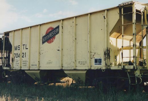 A side view of a cream-colored Chicago and North Western freight car, numbered MS TL 70421, in a grassy yard under a clear sky.