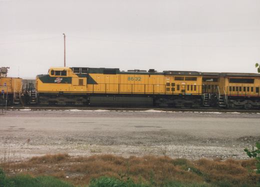 A yellow CNW diesel locomotive, number 8632, is parked on tracks in a snowy rail yard under an overcast sky.