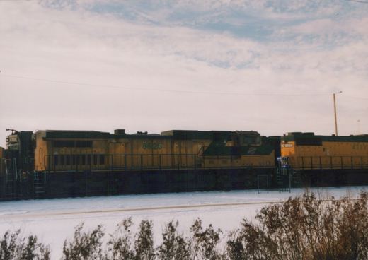 Three yellow and green Chicago and North Western diesel locomotives, numbers 8625, 9754, and 4711, stand in a row on a snow-covered railroad yard under an overcast sky.