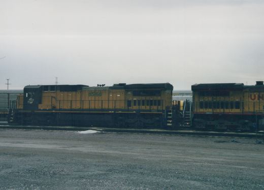 Side view of two diesel locomotives on parallel tracks in a gravel yard, one Chicago and North Western number 8568, the other Union Pacific, under a gray sky with snow patches on the ground.