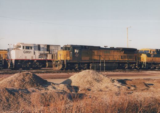 Three diesel locomotives from different railroads are parked side by side in a winter yard, with visible fleet numbers and operator lettering.