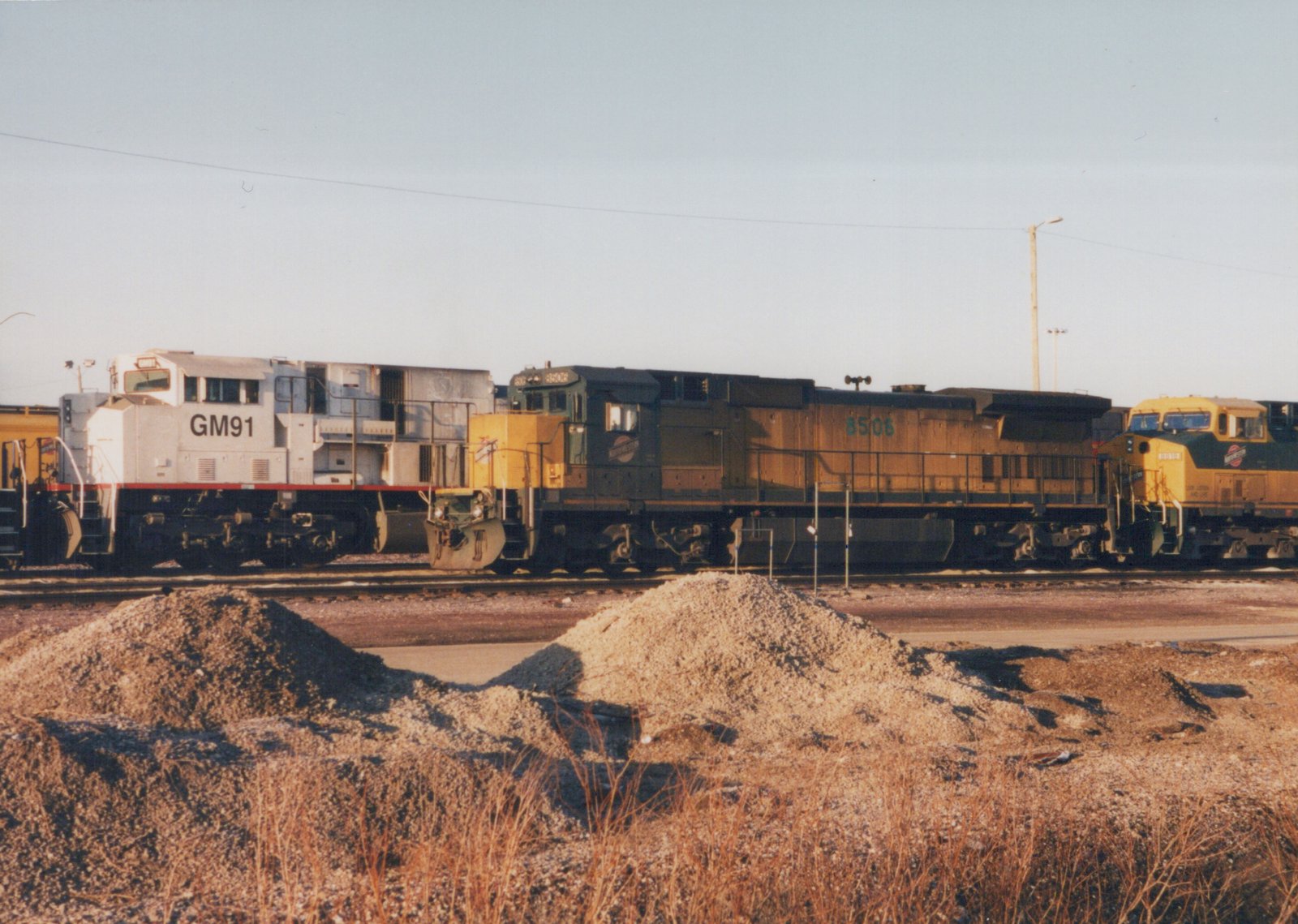 Three diesel locomotives from different railroads are parked side by side in a winter yard, with visible fleet numbers and operator lettering.
