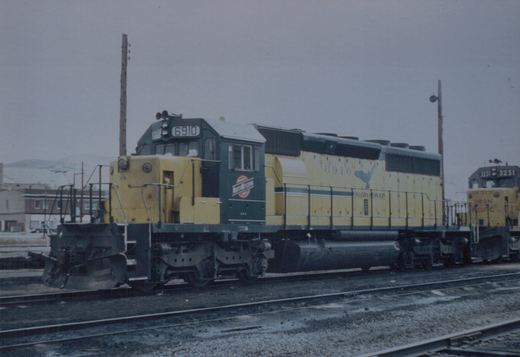 A yellow and green Chicago and North Western locomotive numbered 6910 sits on tracks in a snowy yard, with a Union Pacific locomotive numbered 3231 in the background.