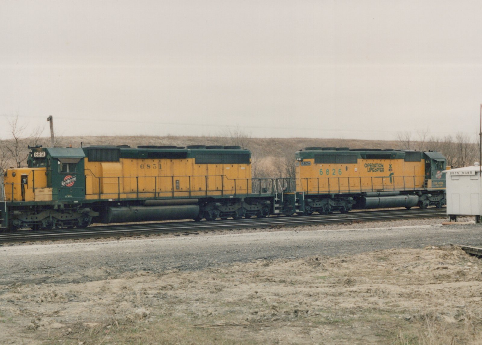 Side view of two yellow and green diesel locomotives coupled on a track with a white signal house labeled 'BRYN MAWR' to the right, in a winter landscape.