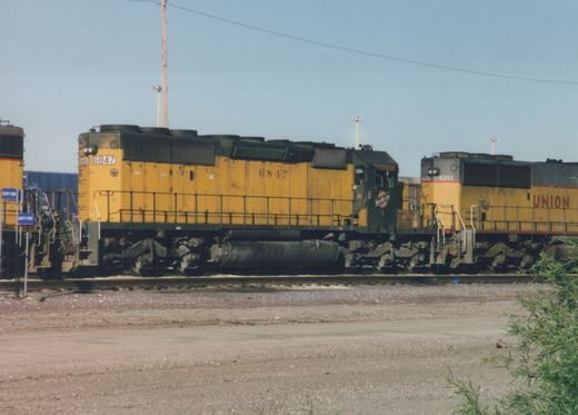Two diesel locomotives, one Chicago and North Western and one Union Pacific, on parallel tracks in a gravel rail yard under a clear sky.