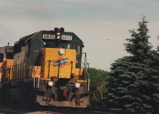Two green and yellow Chicago and North Western diesel locomotives on a track with trees in the background.
