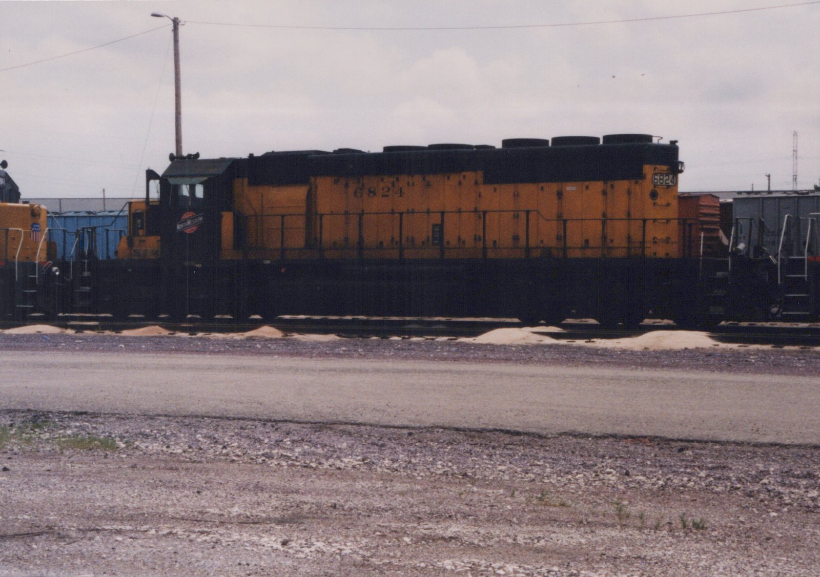 Side view of a yellow and black diesel locomotive numbered 6824 with 'NORTHWESTERN' lettering on the cab, parked on tracks in a gravel yard under an overcast sky.