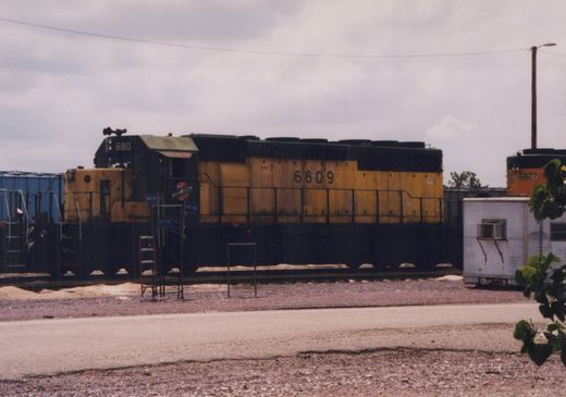 A side view of a yellow and black Chicago and North Western diesel locomotive, number 6809, in a rail yard with another locomotive numbered 6827 in the background.