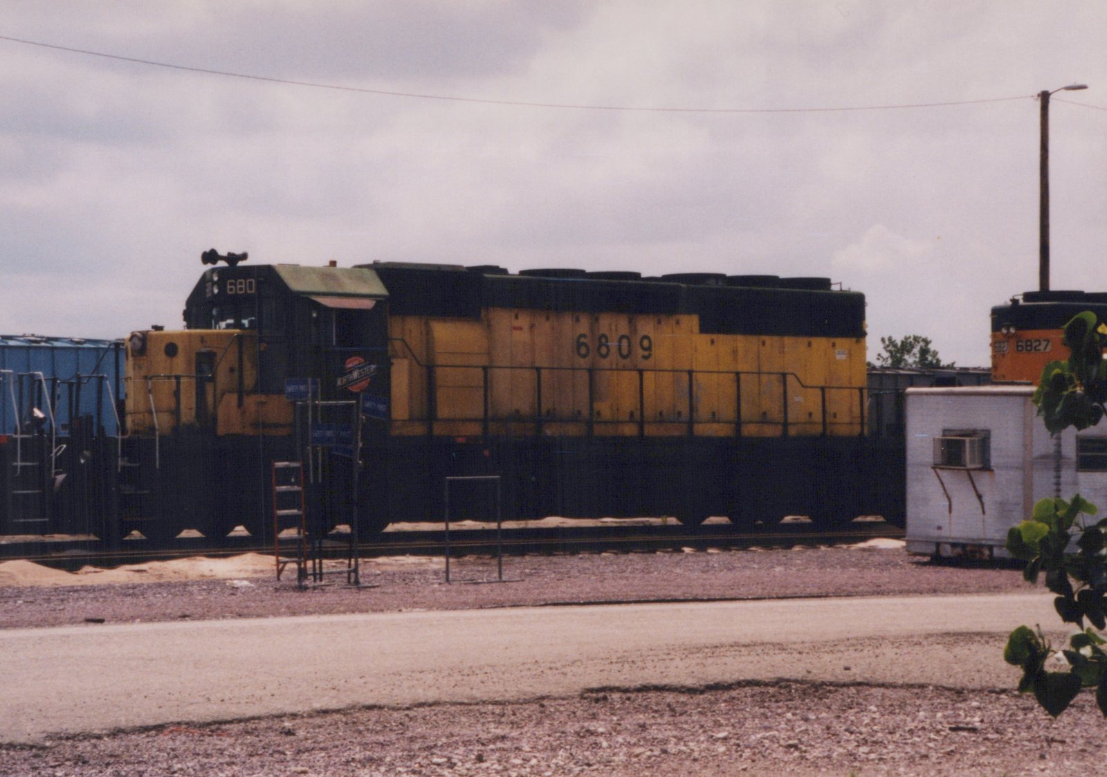 A side view of a yellow and black Chicago and North Western diesel locomotive, number 6809, in a rail yard with another locomotive numbered 6827 in the background.