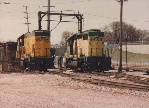 Two yellow and green CNW diesel locomotives, 4405 and 6809, are parked on parallel tracks in a gravel yard under an overcast sky.