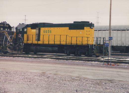 A yellow and green diesel locomotive with the number 6656 on its side is parked on rails next to another black locomotive, with signs reading 'SAFETY FIRST' in the foreground.
