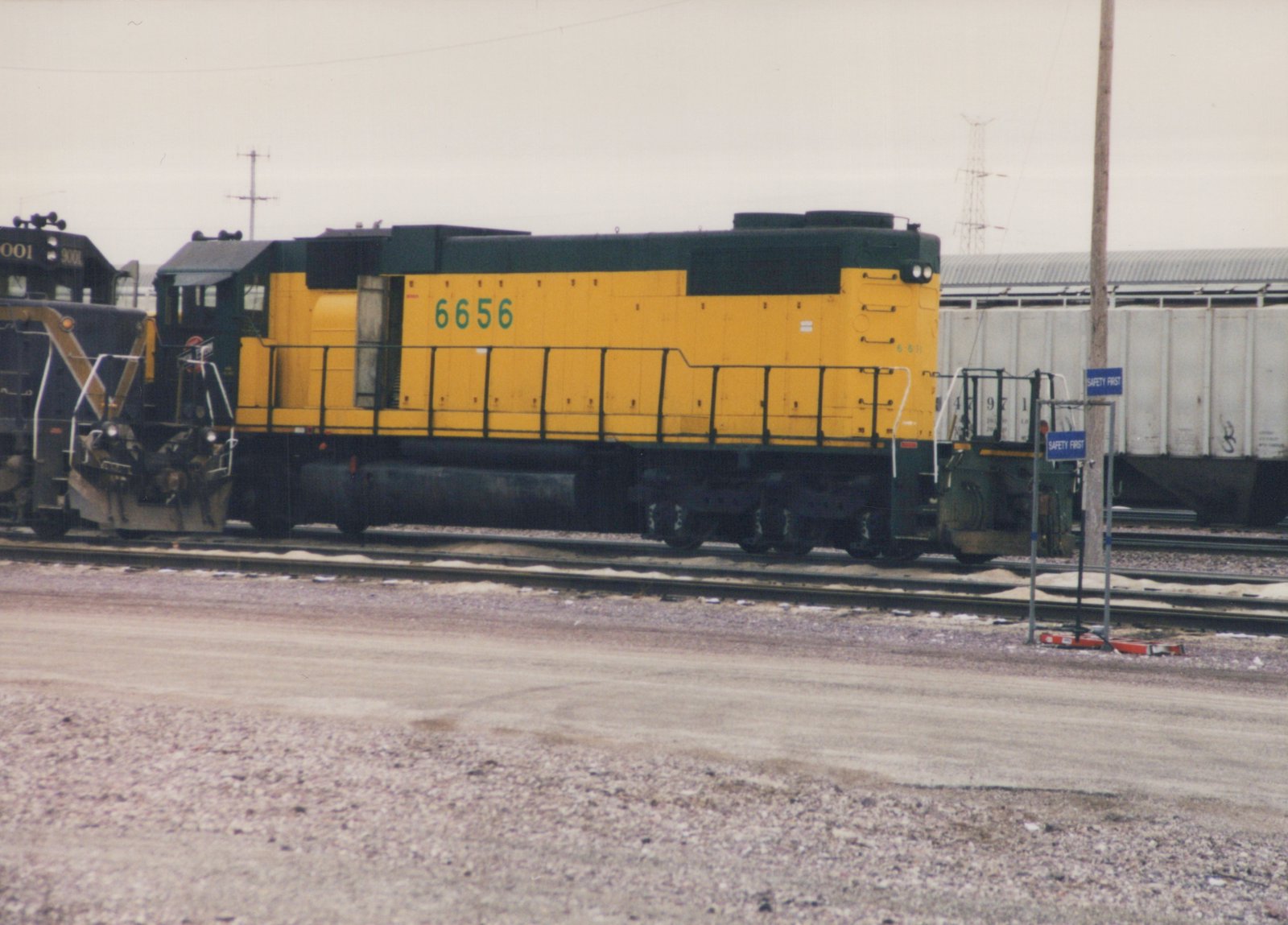 A yellow and green diesel locomotive with the number 6656 on its side is parked on rails next to another black locomotive, with signs reading 'SAFETY FIRST' in the foreground.