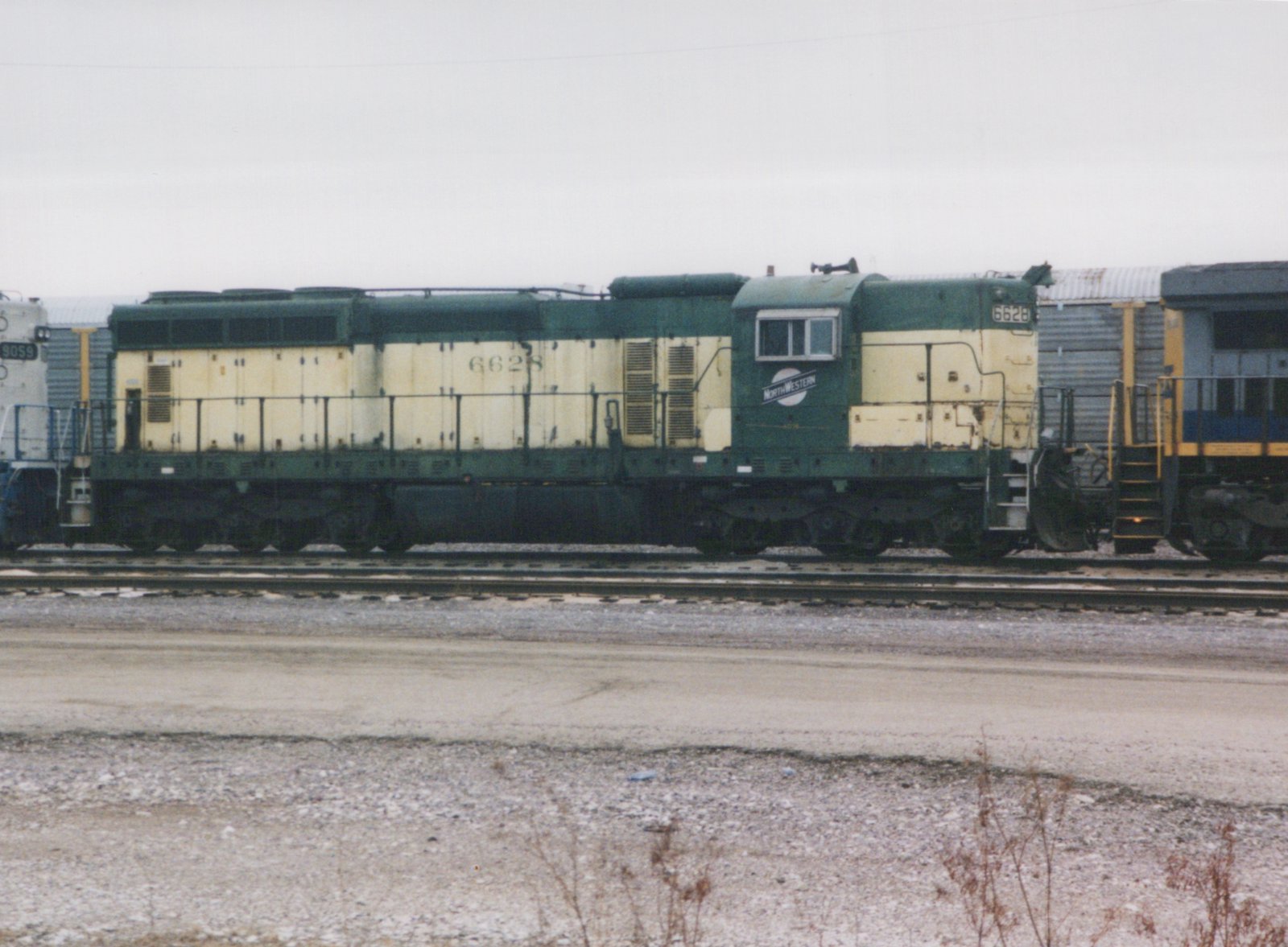Side view of a green and yellow diesel locomotive with the number 6628 and 'NORTHWESTERN' on its cab, sitting on tracks in a rail yard with a gravel foreground.