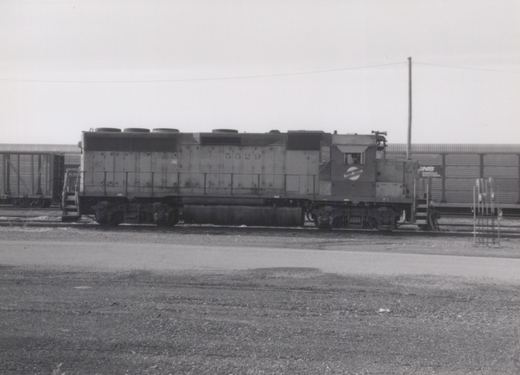 A black and white photograph of a Chicago and North Western diesel locomotive numbered 5529, seen in side profile in a rail yard with freight cars and a gravel foreground.