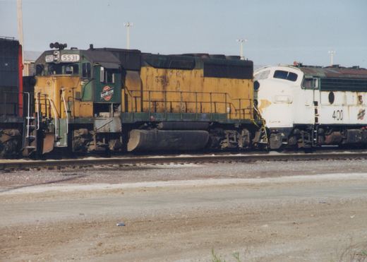 Side view of two Chicago and North Western diesel locomotives, numbers 5531 and 400, parked on tracks in a yard with gravel ground and a clear sky.