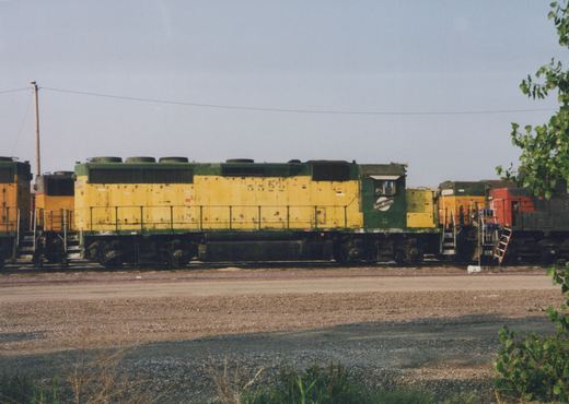 A yellow and green Chicago and North Western locomotive numbered 5522 sitting on tracks in a gravel yard with other locomotives in the background.