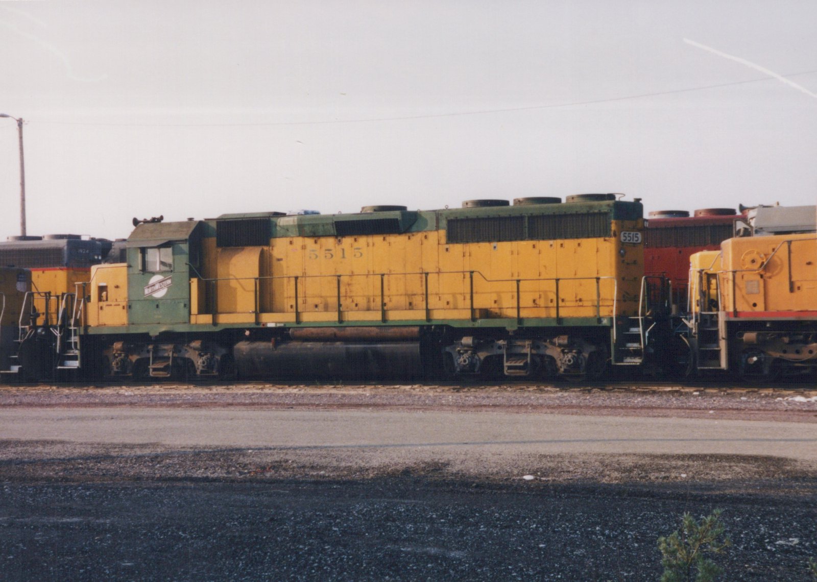 Side view of a C&NW EMD SD24 locomotive, number 5515, in a rail yard, with other locomotives visible in the background.