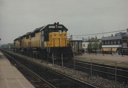 A yellow and black Chicago and North Western diesel locomotive with the number 5057 is stopped at a station platform next to a modern shelter.