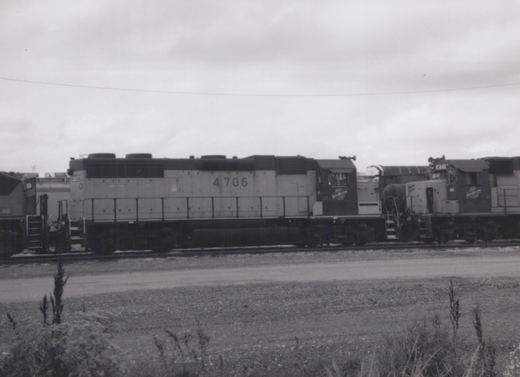 A black-and-white photo shows two gray Seaboard System diesel locomotives, numbers 4706 and 4711, side by side on tracks in a gravel yard with weeds in the foreground.