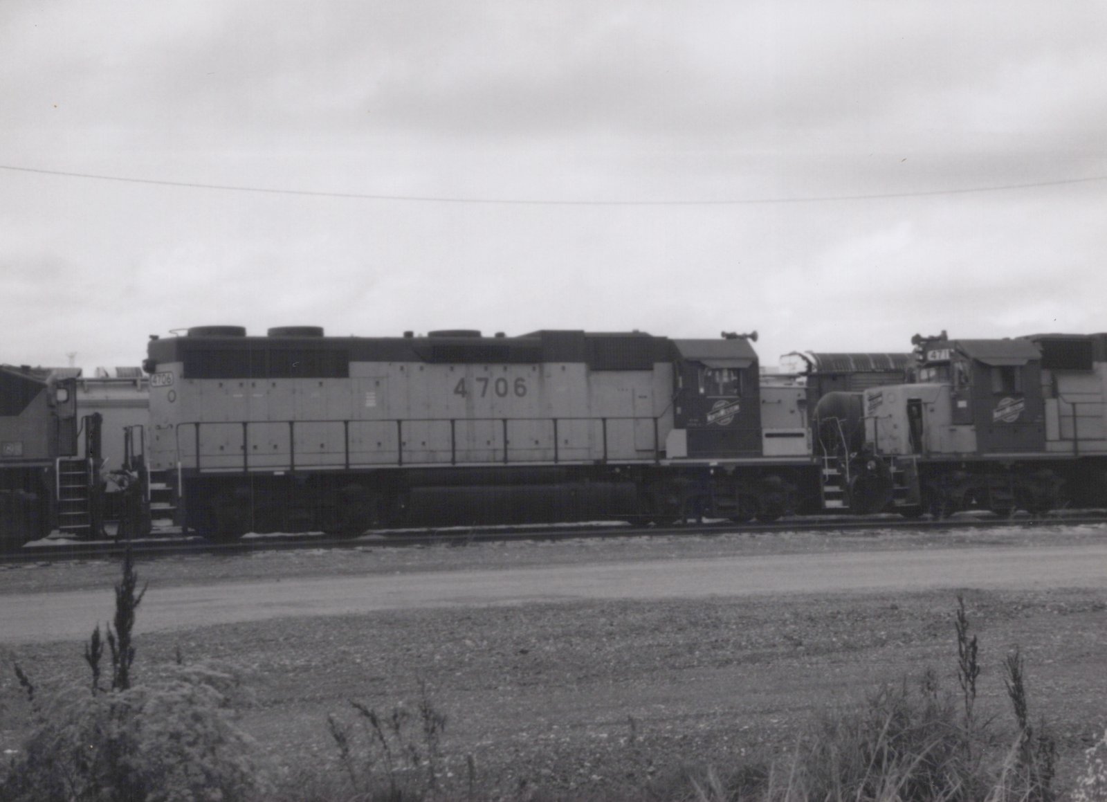 A black-and-white photo shows two gray Seaboard System diesel locomotives, numbers 4706 and 4711, side by side on tracks in a gravel yard with weeds in the foreground.