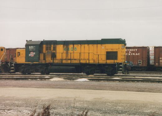 A yellow and green diesel locomotive numbered 4408 is parked on a set of train tracks in a snowy yard with freight cars behind it.