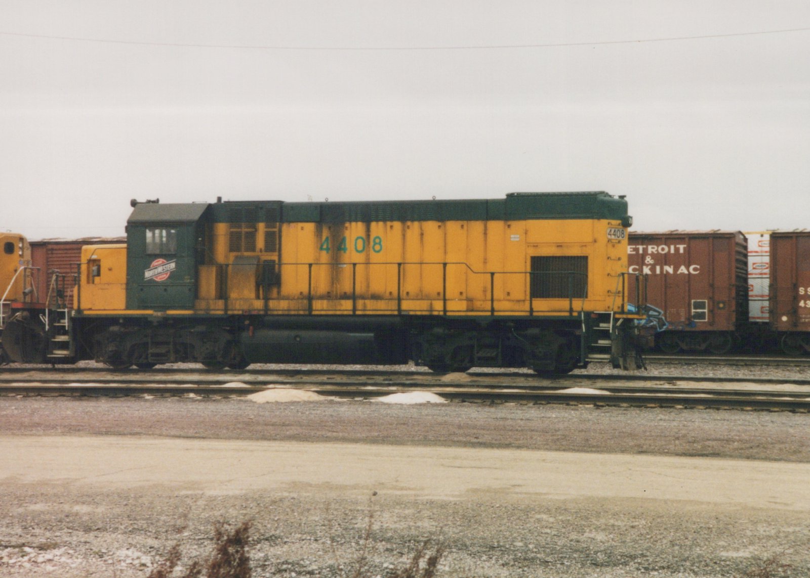A yellow and green diesel locomotive numbered 4408 is parked on a set of train tracks in a snowy yard with freight cars behind it.