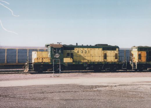 A side view of two green and yellow Chicago and North Western diesel locomotives, numbered 4331 and 4107, parked on tracks in a gravel yard under a clear blue sky.