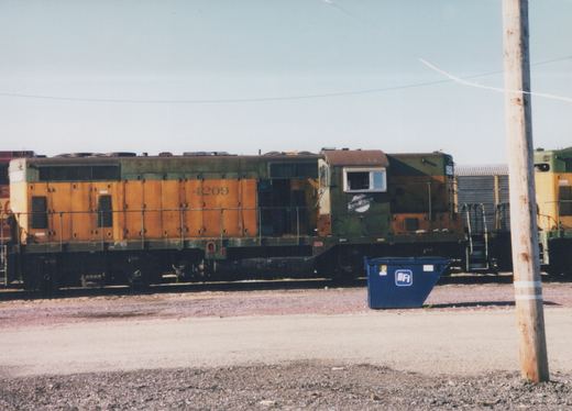 Side view of a Chicago and North Western GP9 diesel locomotive, number 4209, in orange and green, parked on a track in a yard under a clear sky.