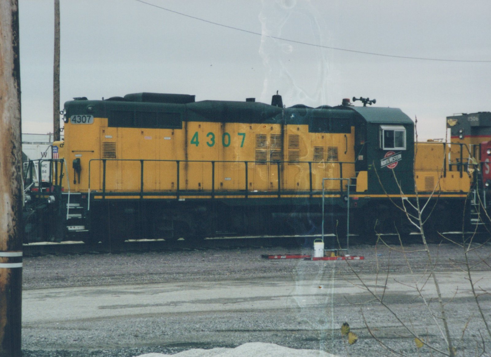 Side view of a yellow and black Chicago and North Western diesel locomotive numbered 4307, parked in a snowy yard with another locomotive behind it.