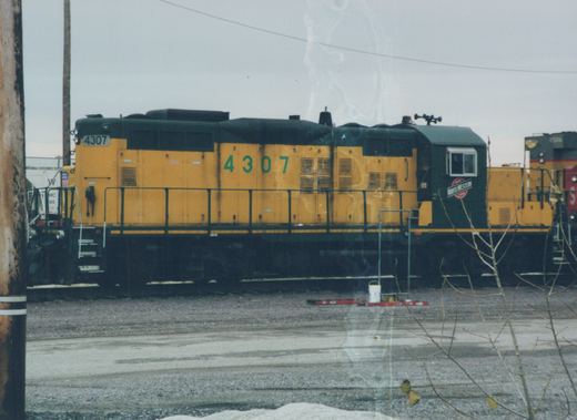 Side view of a yellow and black Chicago and North Western diesel locomotive numbered 4307, parked in a snowy yard with another locomotive behind it.