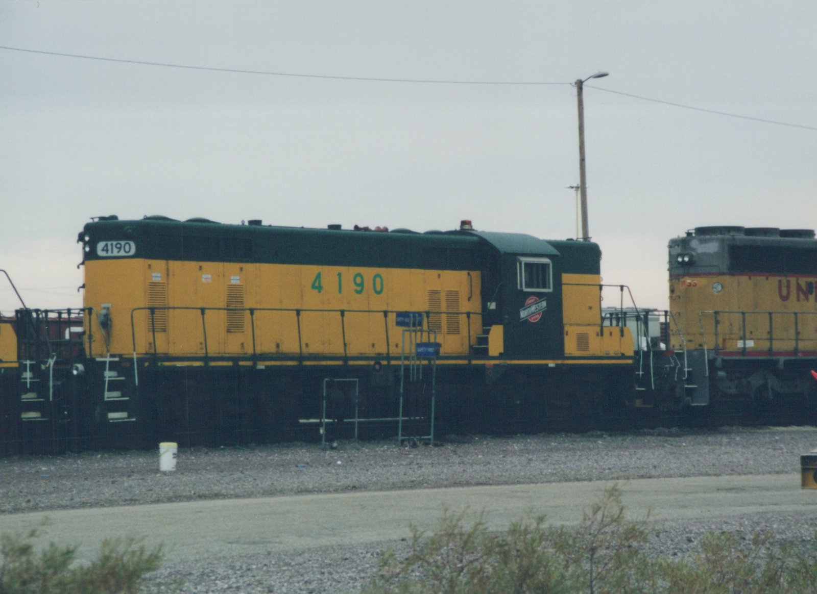 A side view of a yellow and black Chicago and North Western diesel locomotive, number 4190, with a Union Pacific locomotive visible in the background.