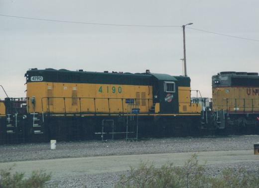 A side view of a yellow and black Chicago and North Western diesel locomotive, number 4190, with a Union Pacific locomotive visible in the background.