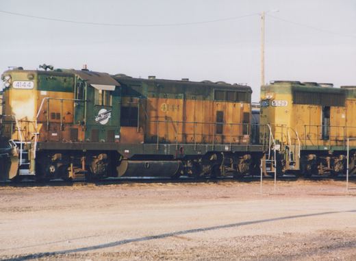 Two green and yellow Chicago and North Western diesel locomotives, one numbered 4144 and the other 5529, are parked next to each other in a gravel yard under an overcast sky.