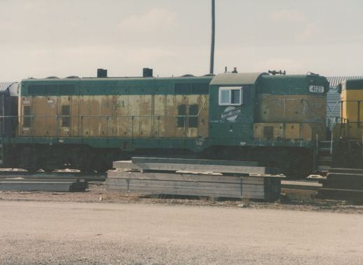 A green and yellow diesel locomotive with the number 4121 and the word NORTHWESTERN on its side sits in a rail yard with stacks of wooden ties in the foreground.