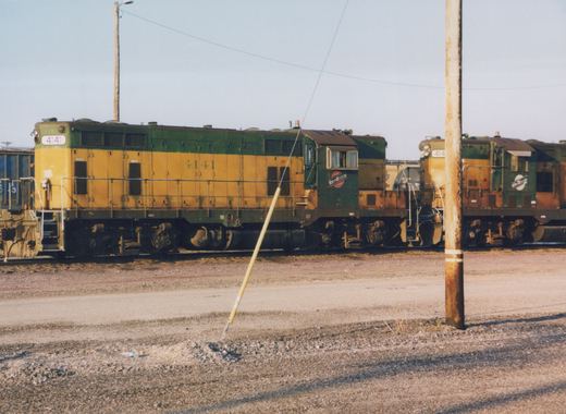 Two Chicago and North Western diesel locomotives, 4141 and 414?, parked in a gravel yard under a clear sky.