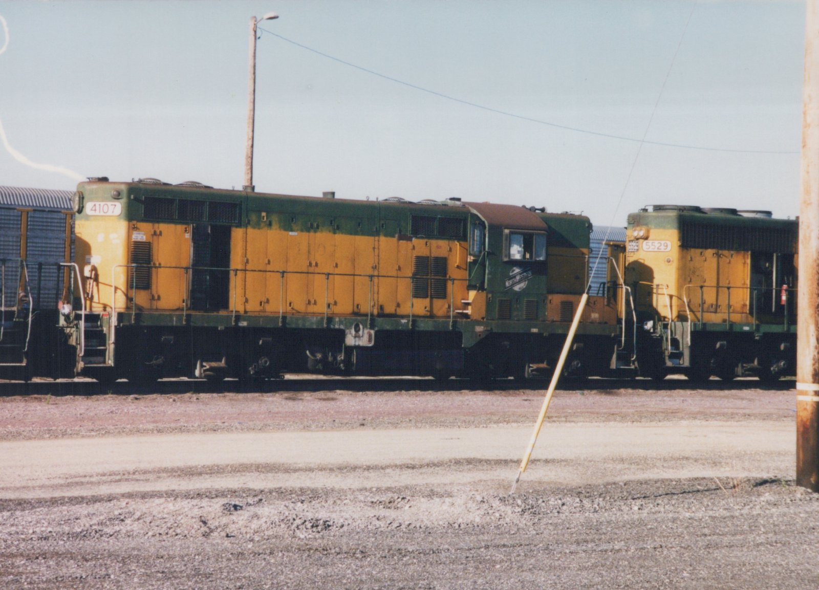 Two diesel locomotives in Chicago and North Western green and yellow livery are parked on parallel tracks in a yard, with number 4107 in front and 5529 behind.