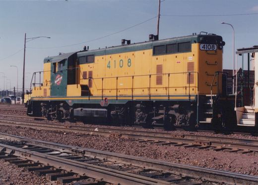 A yellow and green Chicago and North Western diesel locomotive, number 4108, is shown from the side on a set of railroad tracks under a clear sky.