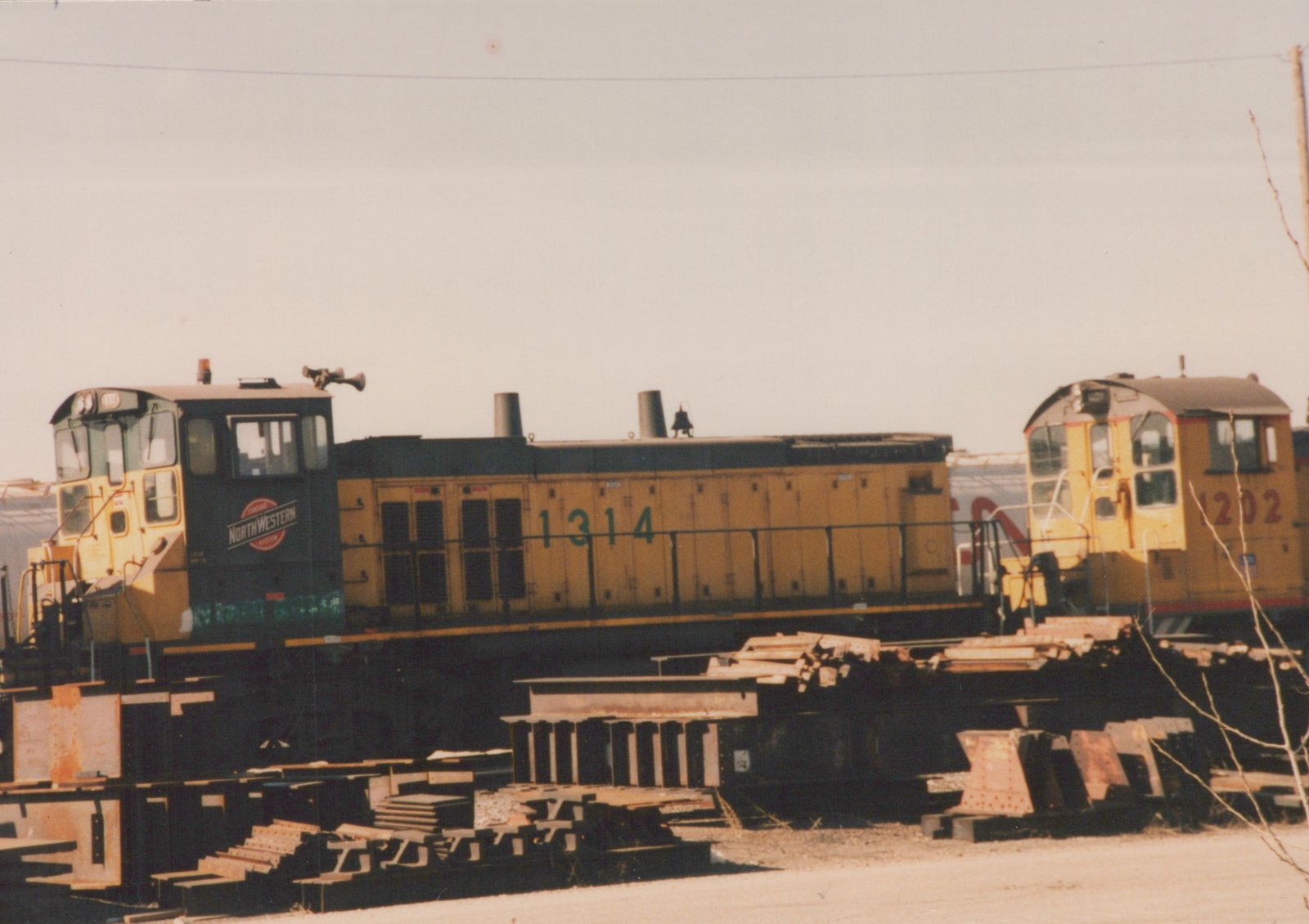 Two yellow and black diesel locomotives with the numbers 1314 and 1202, lettered for the Chicago and North Western Railroad, are parked in a rail yard.