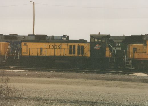 A side view of three Chicago and North Western diesel locomotives, numbered 1309, 6299, and 1510, parked on parallel tracks in a gravel yard on a cloudy day.