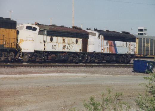 Side view of two white Chicago and North Western diesel locomotives, numbers 400 and 423, parked on tracks in a gravel yard with a blue dumpster nearby and a CSX freight car in the background.