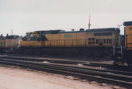 A yellow and green diesel locomotive with the number 8622 and C&NW logo sits on tracks in a rail yard under an overcast sky.