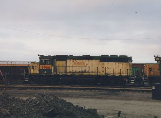 A side view of a green and yellow Union Pacific diesel locomotive with the number 9980 on its front, parked on tracks in a rail yard with another locomotive nearby.