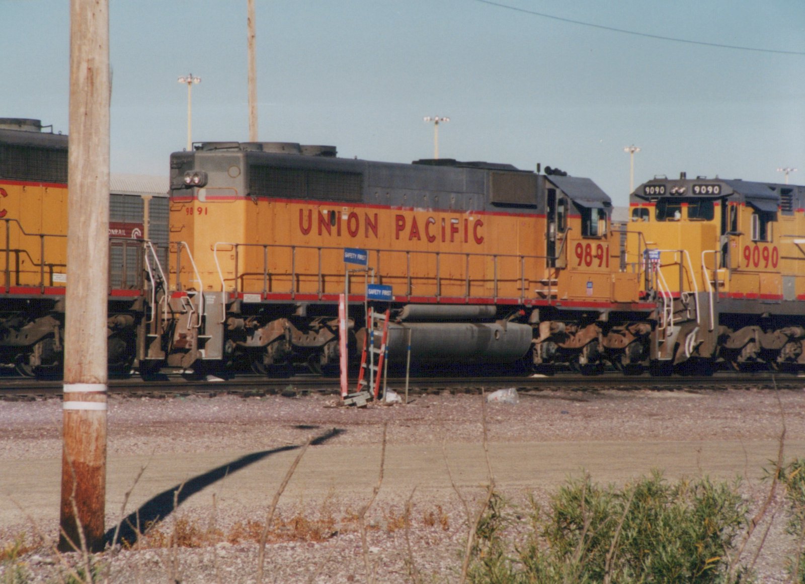 Two yellow Union Pacific diesel locomotives, numbered 9891 and 9090, are parked on parallel tracks in a gravel yard under a clear sky.