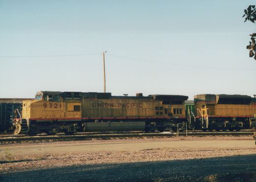 A side view of two yellow Union Pacific diesel locomotives on parallel tracks in a gravel yard under a clear sky.