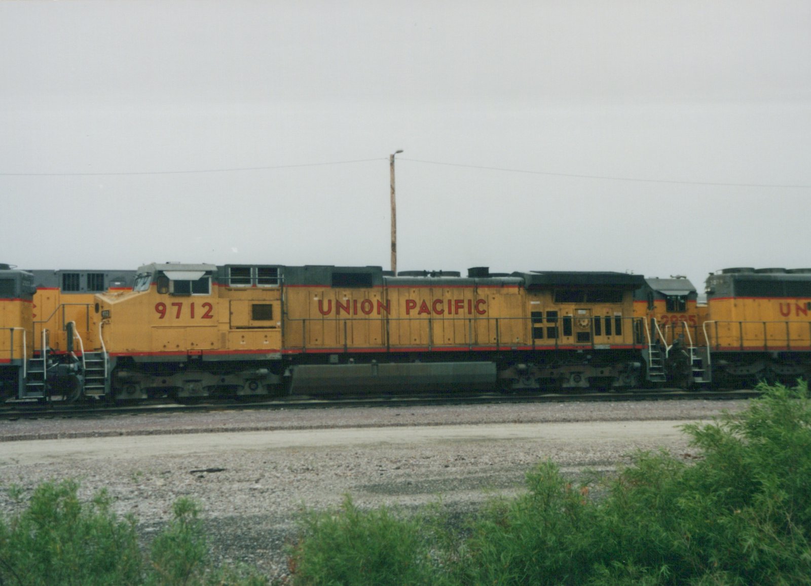 Side view of a yellow Union Pacific diesel locomotive numbered 9712, with two more locomotives of the same model behind it, on a gravel-lined track under an overcast sky.
