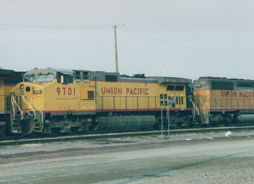 Two large yellow Union Pacific diesel locomotives, numbered 9701 and 3810, sit parked side-by-side on parallel tracks in a gravel yard on a cloudy day.